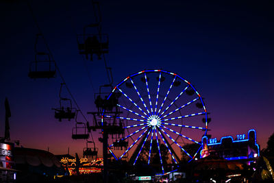 Low angle view of illuminated ferris wheel against blue sky