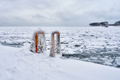 Wooden posts on frozen sea against sky