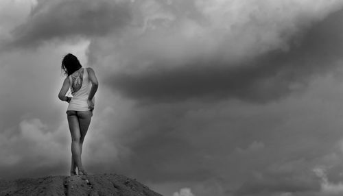 Rear view of woman standing on cliff against sky