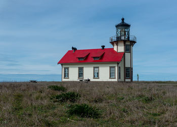 House on field by lighthouse against sky