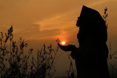 Silhouette woman holding sun against sky during sunset