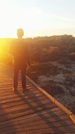 Man standing on footbridge over mountain during sunset