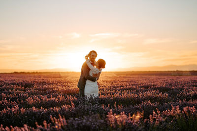 Full length of couple on field against sky during sunset