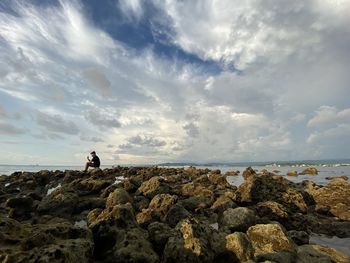 Rear view of man standing on rock by sea against sky