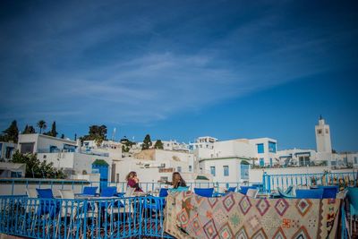 People by swimming pool in city against blue sky