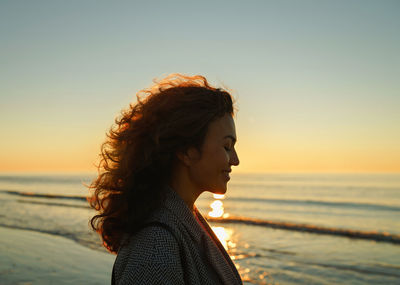 Woman looking at sea shore against sky during sunset