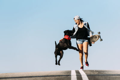 Woman with dog and skateboard against clear blue sky