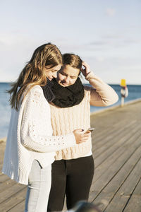 Happy female friends using mobile phone on pier at beach