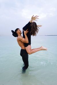 Full length of couple having fun at the beach man lifting his girlfriend 