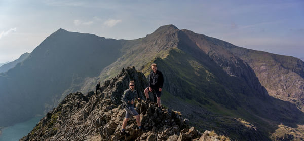 People on rock by mountains against sky