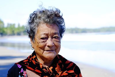 Portrait of senior woman standing at beach against sky