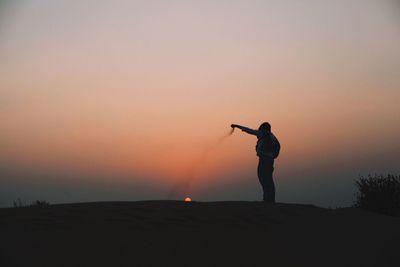 Silhouette of woman standing on landscape at sunset