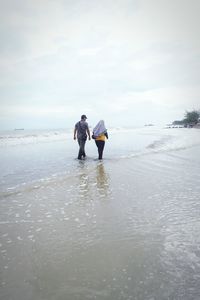 Rear view of men on beach against sky