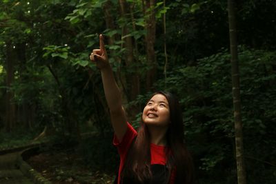 Smiling young woman using mobile phone against trees