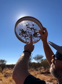 Close-up of man holding strainer on field against clear sky