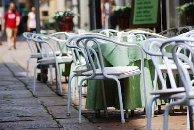 Empty chairs and tables at sidewalk cafe in city