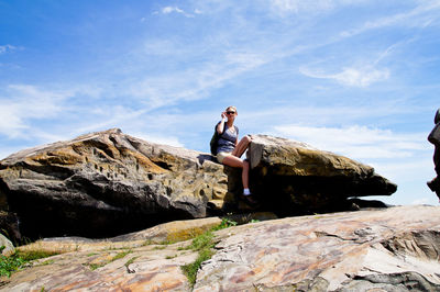 Low angle view of woman sitting on rock against sky