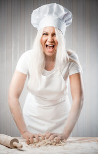 Portrait of young woman screaming while kneading flour in kitchen