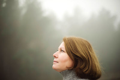 Woman standing by forest in foggy weather