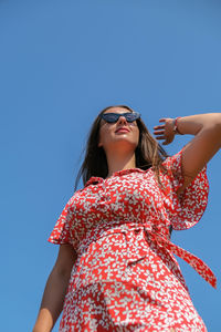 Low angle view of woman wearing sunglasses standing against clear blue sky