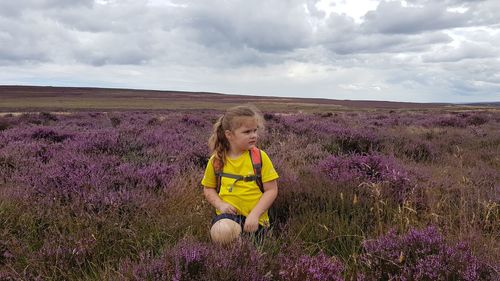 Rear view of girl with yellow flowers on field against sky