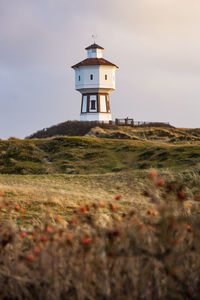 Lighthouse by building against sky