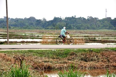 Man riding bicycle on field against clear sky