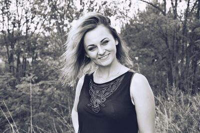Portrait of a smiling young woman standing against trees