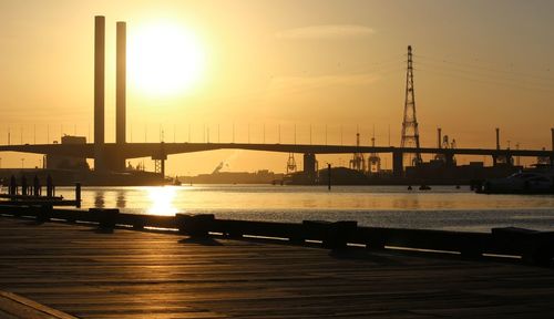 Silhouette bridge over river against sky during sunset