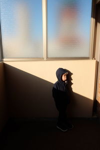 Side view of young woman sitting on window at home