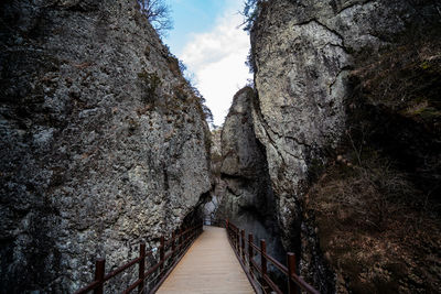 Narrow footpath amidst rocks against sky