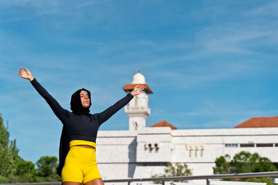 Woman with arms raised standing against building