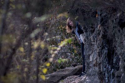 Portrait of woman hiding behind rock in forest
