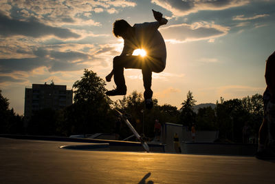 Silhouette man jumping in swimming pool against sky during sunset