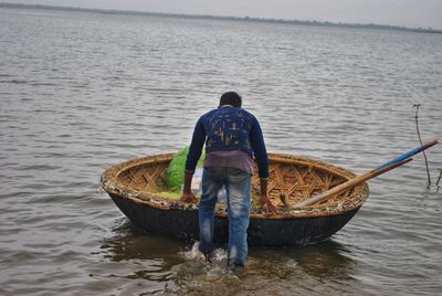 Rear view of man standing on boat in sea
