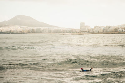 Man in sea by city against sky