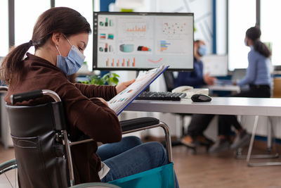 Businesswoman wearing mask looking at graph at office