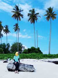 Woman sitting on log at beach against palm trees