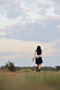 Rear view of woman walking on field against sky