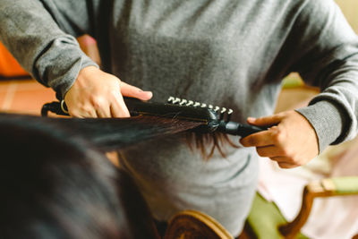 Midsection of hairstylist using curler on woman hair in salon