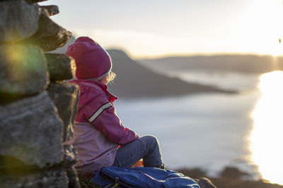 Woman sitting on rock looking at mountain against sky