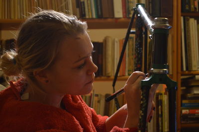 Woman painting bicycle frame against bookshelf