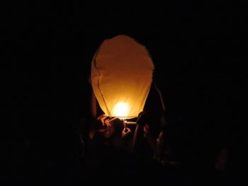 Silhouette people on illuminated lantern against black background