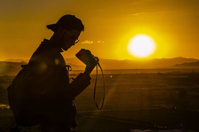 Silhouette man photographing at sunset