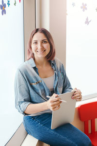 Portrait of smiling young woman sitting by window