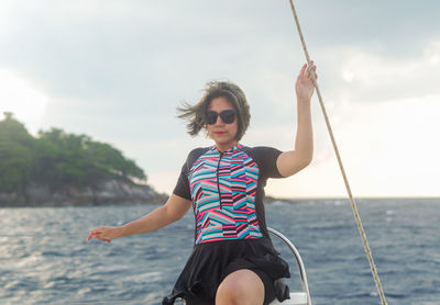 Portrait of young woman swinging at beach against sky