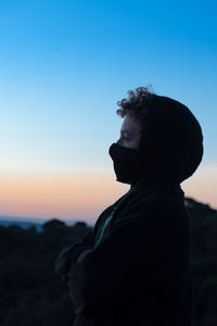Side view of boy wearing flu mask standing against sky at dusk