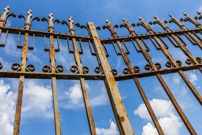 Low angle view of metal fence against blue sky