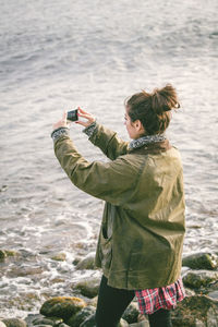 Woman photographing sea while standing on shore at beach