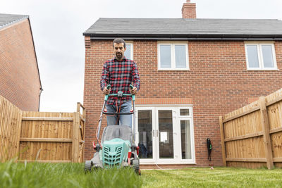 Mid adult man using lawn mower for mowing at backyard